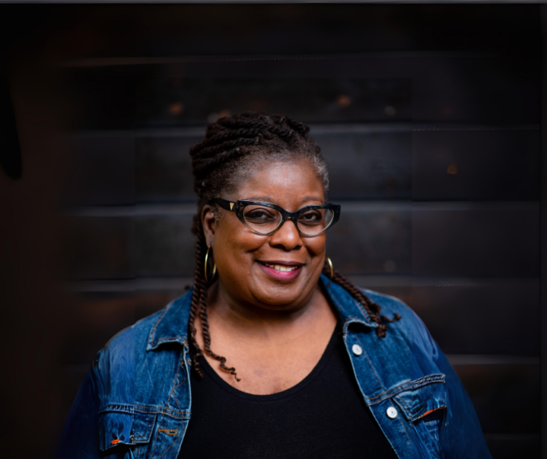 Headshot of Sheryl Wilson in black top with denim blue overshirt