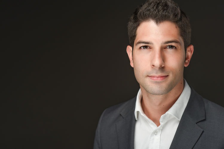 Nicholas Susi in white shirt with dark coat against a black background