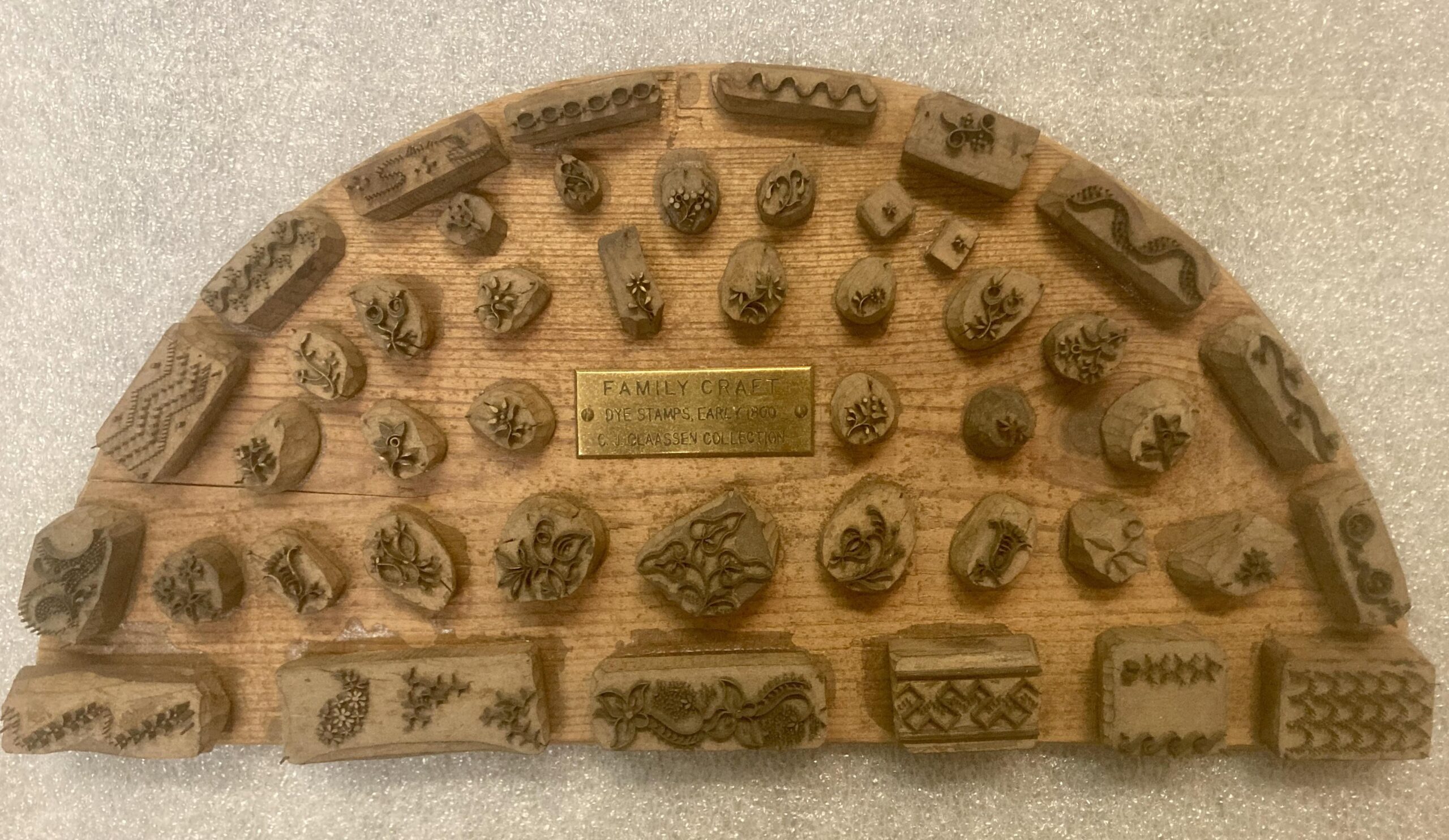 A half-circle wood block with raised stamps used to decorate hand-made aprons, from the late 19th/early 20th century.