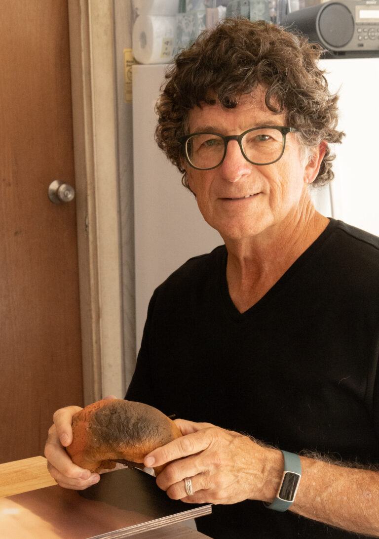 Merrill Krabill in black shirt, holding a piece of ceramic sculpture