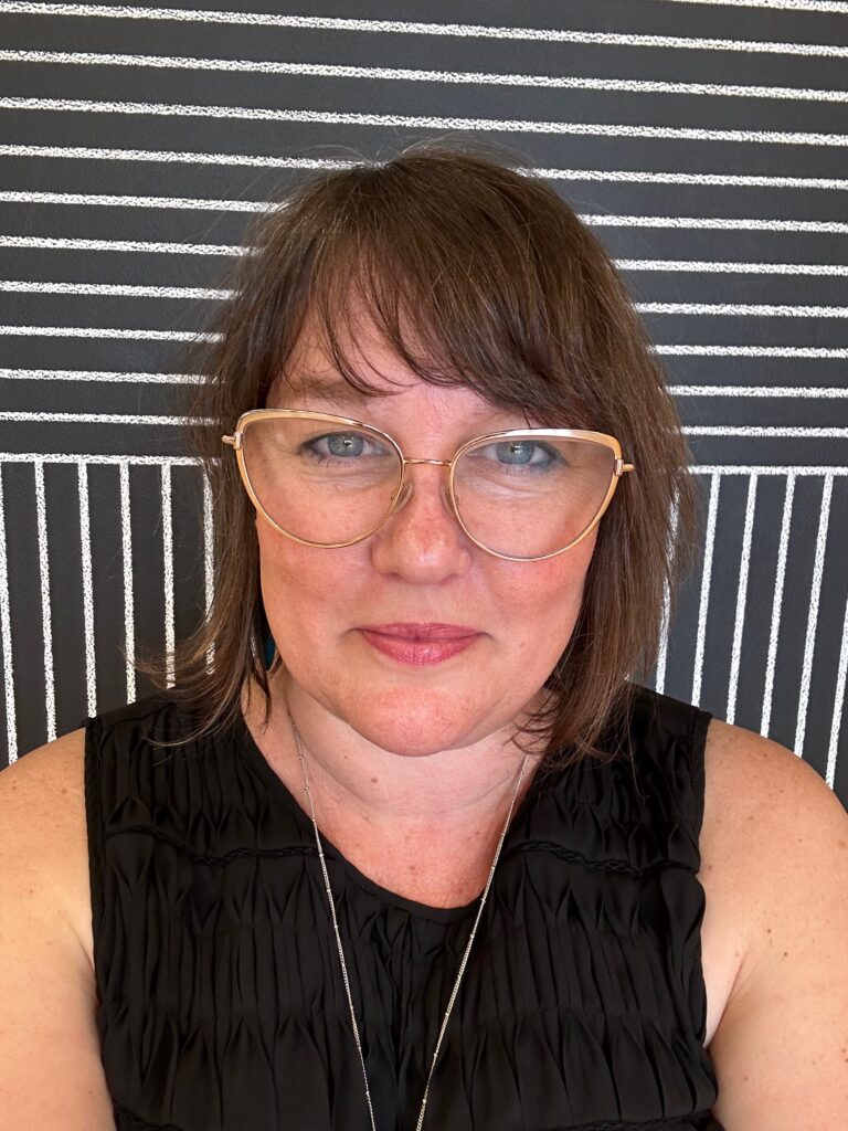 Headshot of white woman wearing glasses, wearing a sleeveless black top, in front of a window or porch screen