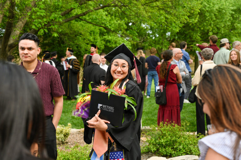 Graduate in cap and gown, holding diploma in its case and an armful of flowers