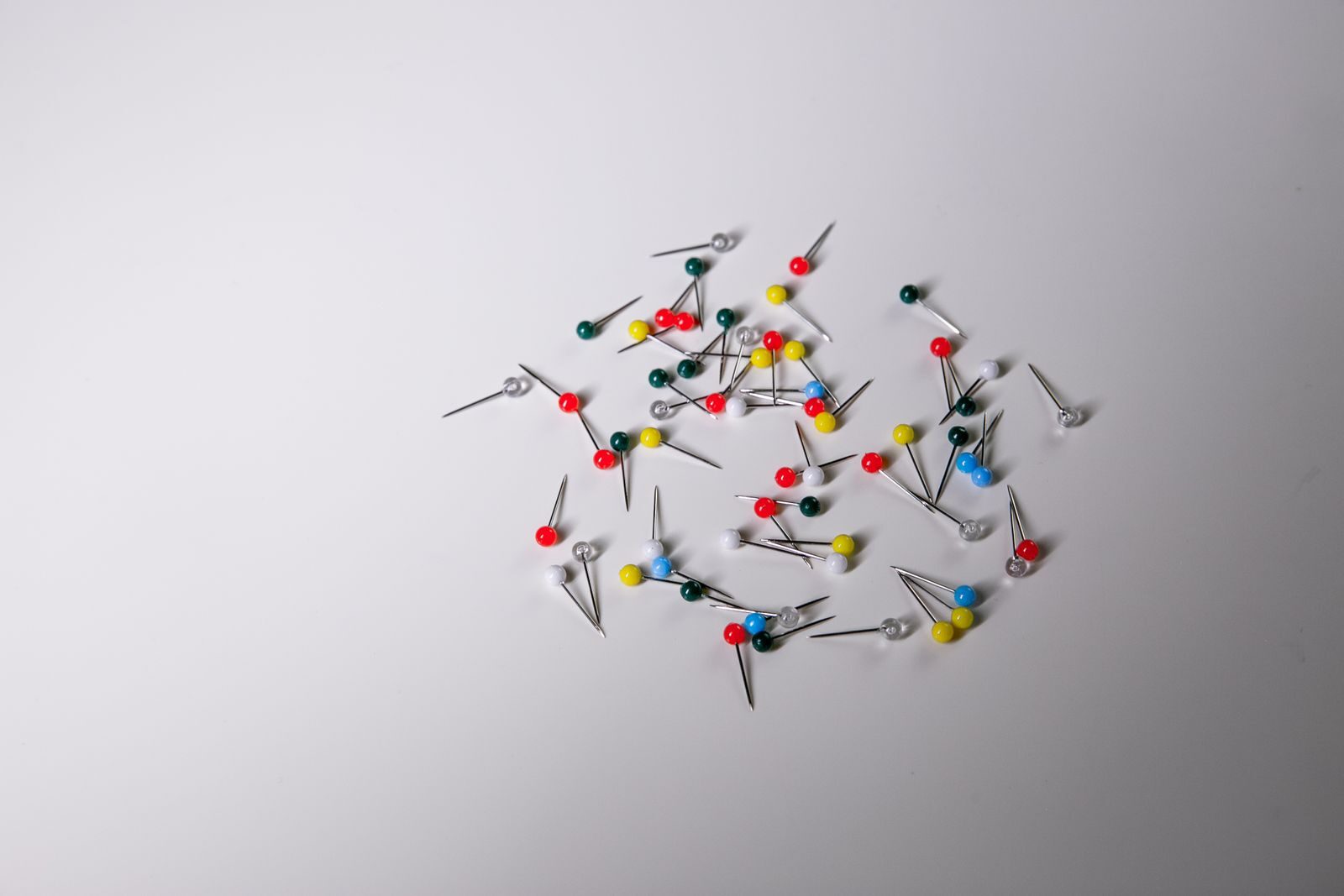 Scattered colorful push pins on a plain white surface, ideal for office and creative concepts.